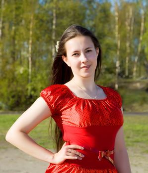 portrait of a beautiful girl in a red dress with her hair in the background of green foliage