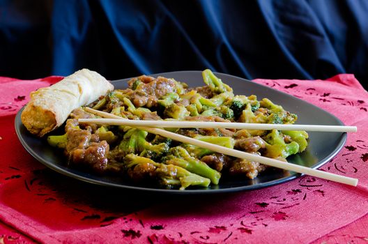 Beef with broccoli with spring roll and chop sticks.