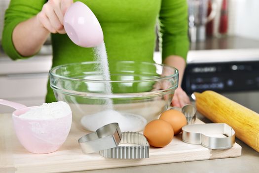 Pouring sugar into mixing bowl with ingredients for making cookies