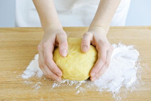 Hands kneading ball of dough with flour on cutting board