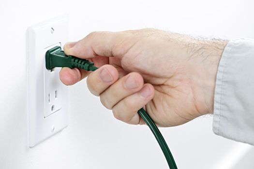 Hand pulling green electrical plug from outlet