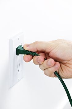 Hand pulling green electrical plug from outlet