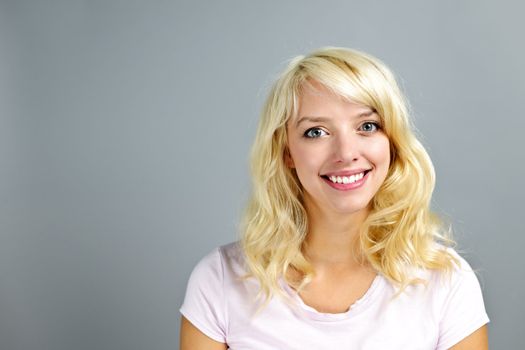 Portrait of smiling young blonde caucasian woman on grey background