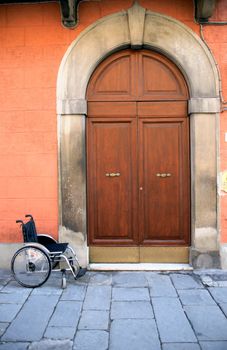 Urban scene. Empty wheelchair near old house with nice vintage wooden door