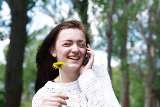 Smiling beauty teenage girl with dandelion talking on mobile phone