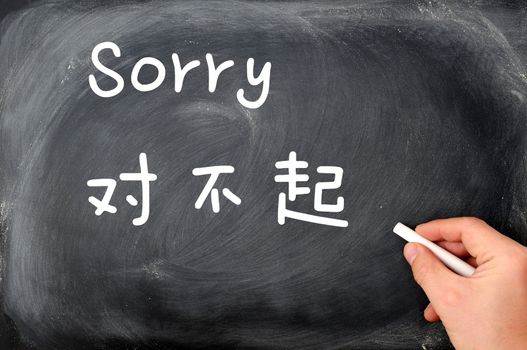 "Sorry" written on a blackboard background with a Chinese version, with a hand holding chalk.