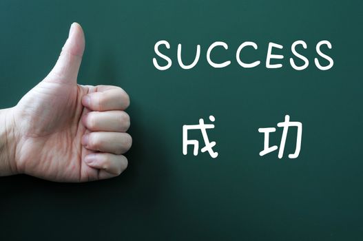 "Success" written on a blackboard with a Chinese version and with thumb up