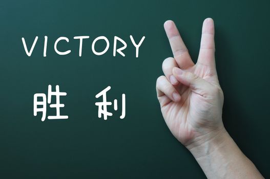 Victory gesture on a blackboard background, with the word victory written in both English and Chinese