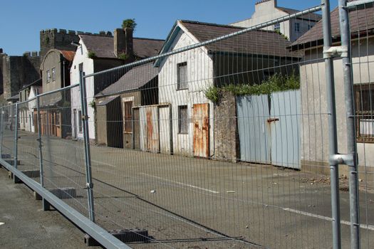 A row of condemed abandoned derelict buildings with a metal security fence.