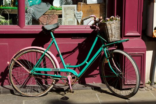 An old pink and green  painted bicycle with a basket leaning against a window.
