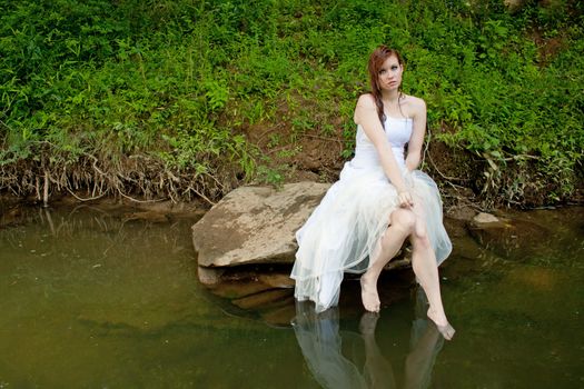 Wet bride sitting on a rock over the water