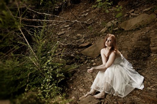A sad but beautiful bride sitting on a rocky hillside