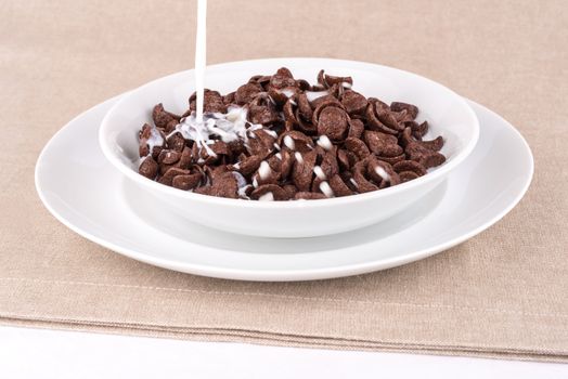 Milk pouring into a dish with chocolate cereal flakes.