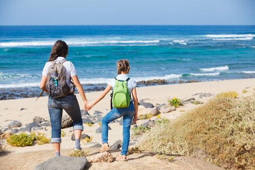 Back view of mother with her daughter walking on a beach, wearing jeans and white shirts