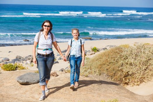 Mother with her daughter walking on a beach, wearing jeans and white shirts