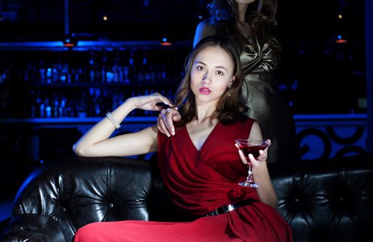 young woman has a rest with an alcoholic drink, second woman on a background