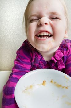 High key tight cropped shot of a single child making a funny smily face when she finished her food