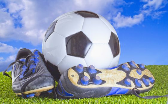 White and black football with shoes, over grass and blue sky