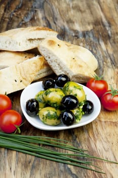 green olives with fresh bread and herbs on wooden background