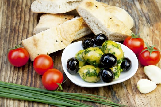 green olives with fresh bread and herbs on wooden background