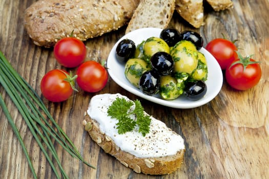 green olives with fresh bread and herbs on wooden background