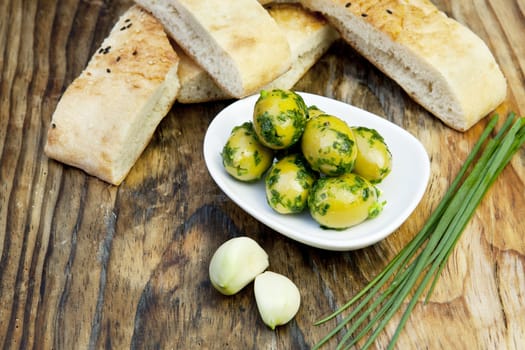 green olives with fresh bread and herbs on wooden background