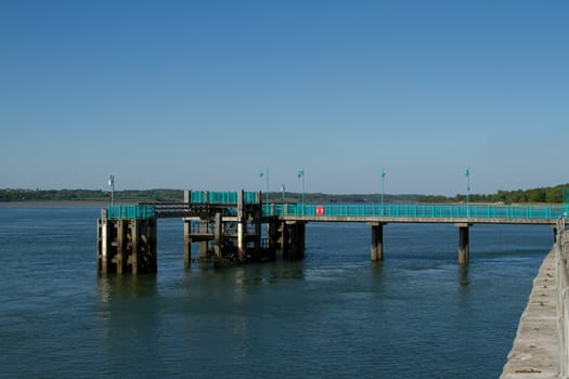 A small dock, landing point, in the sea with a walkway painted green with railings.