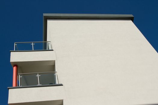 A building painted cream with a flat roof and balconies with a post, railings and glass panels against a blue sky.