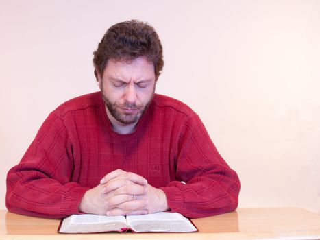 Man in red sweater praying and reading the bible.
