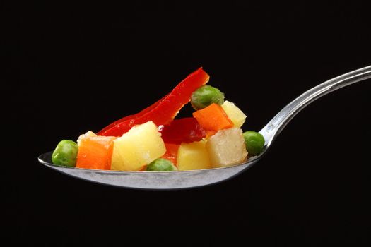Frozen vegetables in a spoon over black