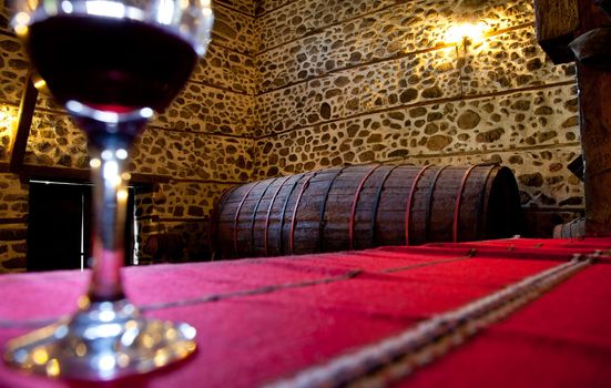 glass with red wine in wine cellar, focus on barrel