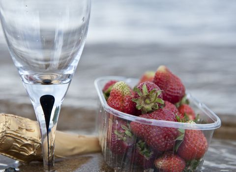 Cloesup of some strawberries a glass and a bottle of wine by the seaside