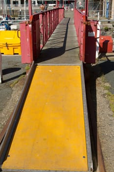 A footbridge with red metal railings wooen floor and a yellow ramp providing access.