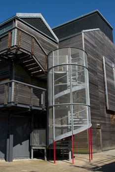 A wooden faced building with a caged spiral stairs, leading up the outside.