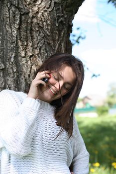 Smiling beauty teenage girl near tree talking on her mobile phone