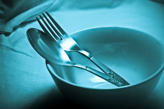Stainless steel spoon and fork in an empty ceramic bowl