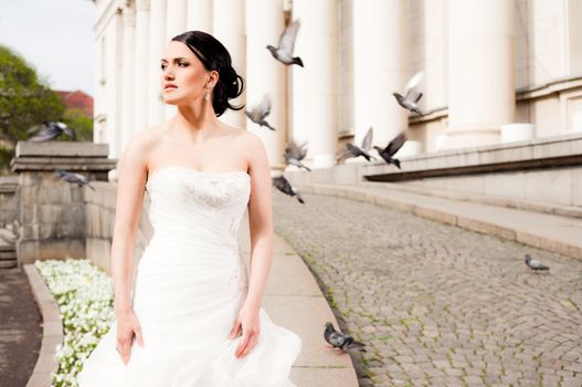 Beautiful bride standing outdoors looking right, doves flying behind her