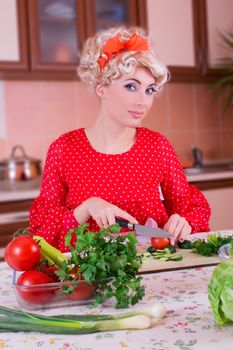 Pinup woman in red cutting vegetables in kitchen