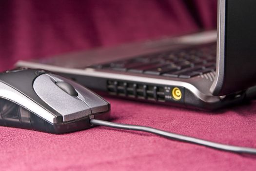 The grey computer mouse and modern laptop on a claret background