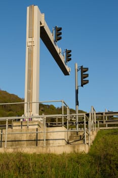 A set of traffic lights with a concrete walkway and railings against a clear blue sky.