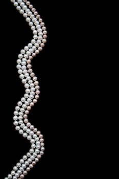 White and pink pearls on the black silk as background 