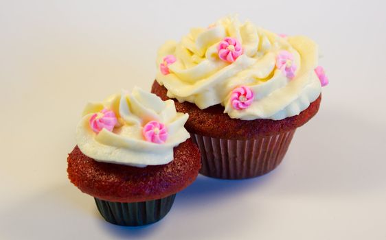 Red velvet cupcakes with buttercream icing with flower decorations isolated on white.