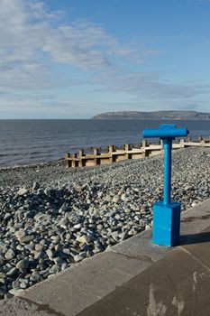 A blue telescope placed on a walkway next to a pebble beach with an island in the distance.