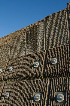 An engineered precast concrete retaining wall with stainless steel reinforcing pins against a blue sky.