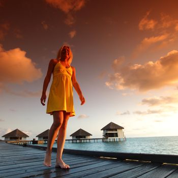 woman in a dress on a bridge home sea and the maldivian sunset on the background