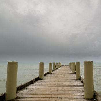 Wooden marine pier with large side bollards receding straight into the distance over the ocean on an overcast day