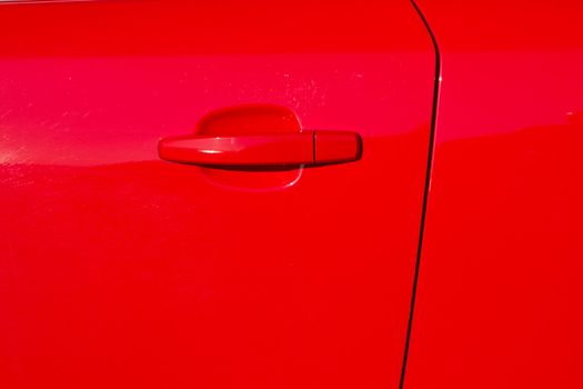 A glossy red painted car door with door edge and a handle.