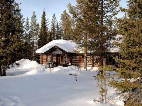 Romantic snow covered log cabin between the trees in a holiday resort in Lapland, Finland.