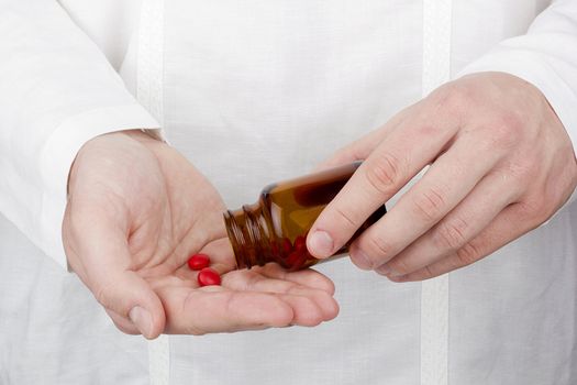 Close-up photograph of a hand pouring red tablets out of a transparent bottle into another hand.