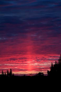 Very colorful sun pillar at sunset paints the sky